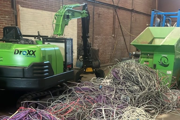 Groene machine naast een berg gesloopte kabels in een grote, lege ruimte.